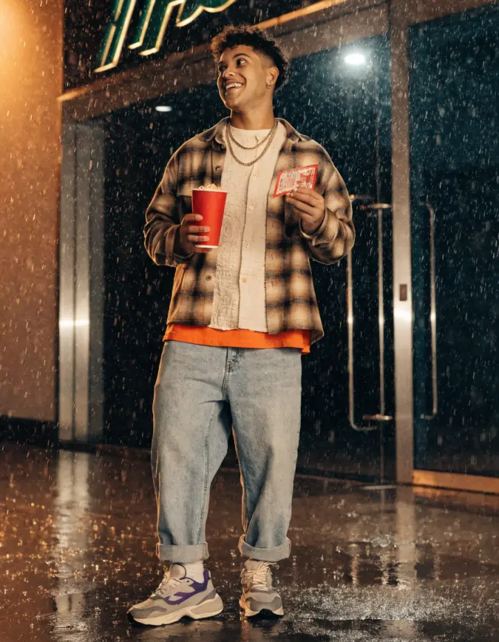 Jovem sorrindo com pipoca e ingresso na porta do cinema